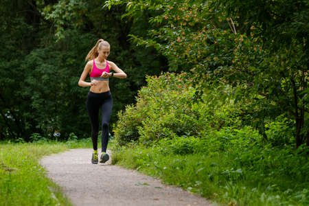 Young slim woman jogging in a park looking to smart watch