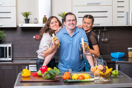 Two young women are fed bananas midle age man in the kitchenの写真素材