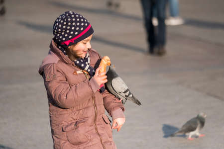 Krakow, Poland - December 20, 2016: Girl age 6-8 years feeding pigeons at main square in old city at day timeのeditorial素材