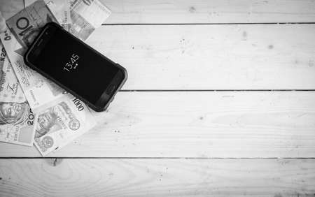 Banknotes different countries on the wooden table under the smartphoneの写真素材