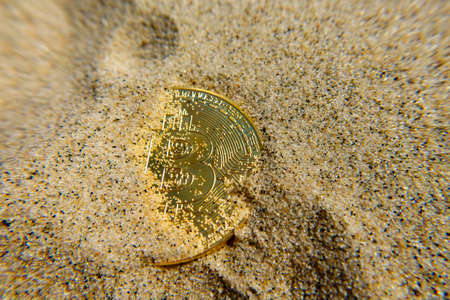 Golden bitcoin coin in the sandの写真素材