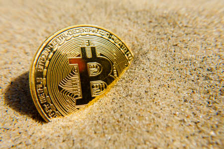 Golden bitcoin coin in the sandの写真素材