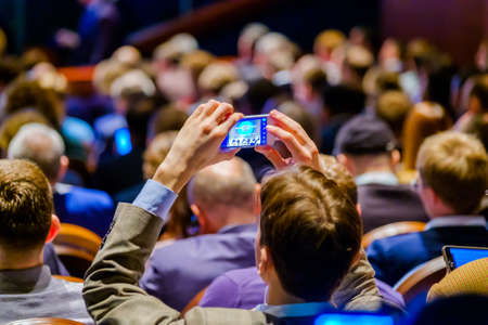 Man takes a picture of the presentation at the conference hall using smartphoneの写真素材
