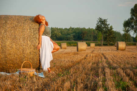 Red-haired woman posing on the field near a haystack