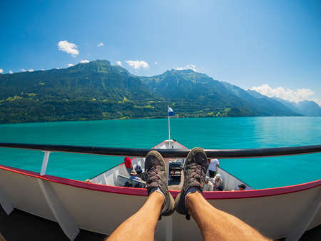 POV travelling by boat at Brienz lake at summer time in Switzerland. Tourists feet at foreground