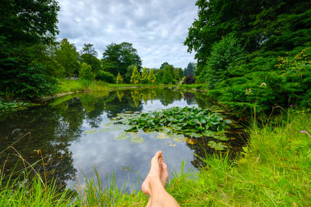 Summer landscape of pond in park male feet in foreground.の写真素材