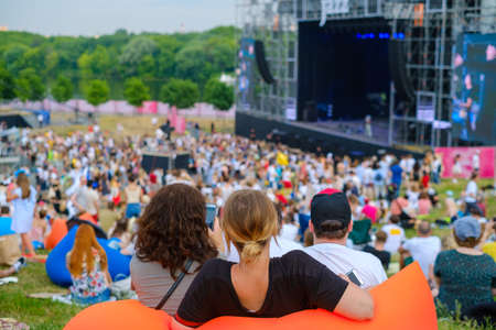 Friends watching concert at open air music festival, back view, stage and spectators at background