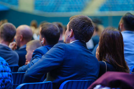 Business conference attendees sit and listen to lecturer, rear view