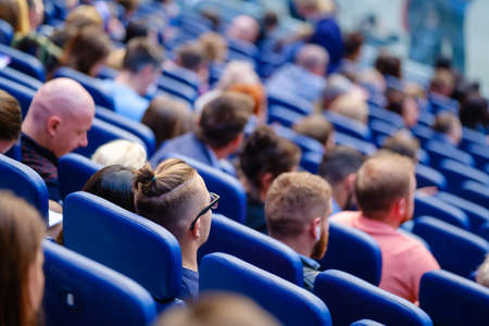 Business conference attendees sit and listen to lecturer, rear view