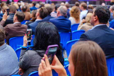 Business conference attendees sit and listen to lecturer, rear view