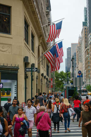 New York, USA - August 12, 2019: People crossing road at 5th Avenue near building with flags on...