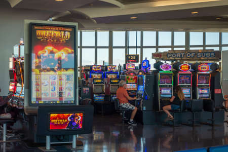 Las Vegas, USA - August 12, 2019: Unrecognizable travelers playing modern slot machines in airport...