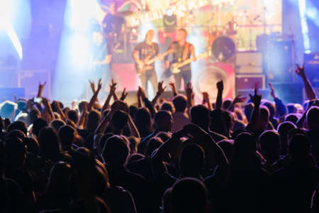 Silhouettes of people enjoying live concert of musician band performing song on stage in bright spotlightsの写真素材