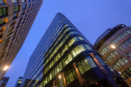 From below illuminated high rise buildings located against cloudless sky in evening on street of...