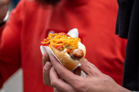 Unrecognizable guy holding tasty hot dog wrapped in paper while standing in crowd on city streetの写真素材