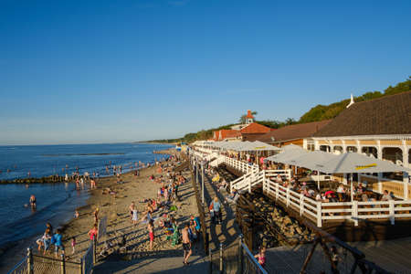 Zelenogradsk, Russia - August 20, 2020: People spending sunny summer evening on sandy beach with outdoor cafe near sea waterのeditorial素材