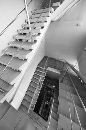 Black and white tiled stairway with metal railing leading down inside contemporary buildingの写真素材