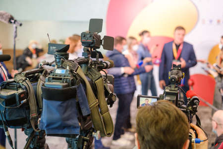 Professional cameras shoot male entrepreneur speaking with reporters during business seminar in modern hallの写真素材