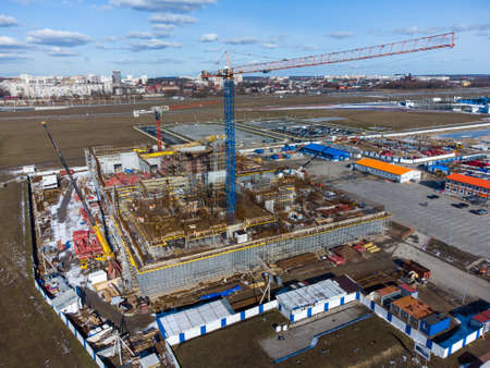 Drone view of tall crane located in middle of construction site near unfinished building in city outskirtsの写真素材