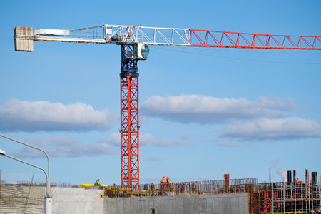 Tall crane located near unfinished building walls with builders against cloudy blue sky on...
