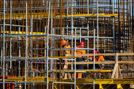 Back view of anonymous men in uniform walking near wooden railing and metal poles during work on construction siteの写真素材