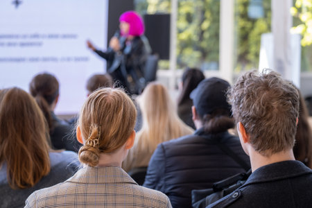 Group of businesspeople sitting in hall and listening to female speakerの写真素材