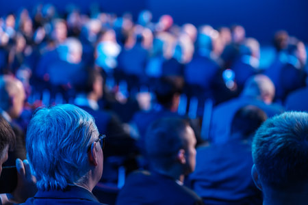 Businessmen listening to speaker giving presentation in illuminated auditorium at export forumの写真素材