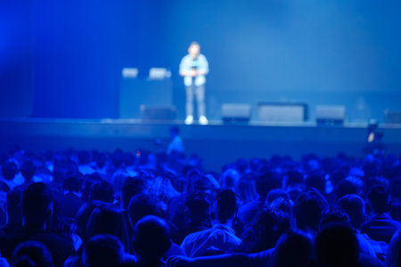 Back view of businesspeople watching speaker on stage in blue illuminated stadiumの写真素材