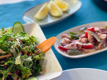 A healthy Mediterranean salad next to grilled octopus on a table, showcasing fresh dining options.の写真素材