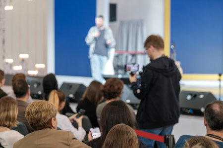 Defocused image of a speaker at event with audience watching intently, capturing the atmosphere of live presentations.の写真素材