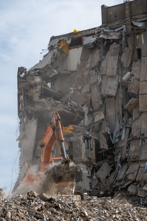An orange excavator actively demolishing a severely damaged building, surrounded by rubble and...