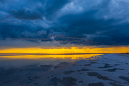 Dramatic sunset over a tranquil ocean with dark clouds reflecting on the water. The striking sky...