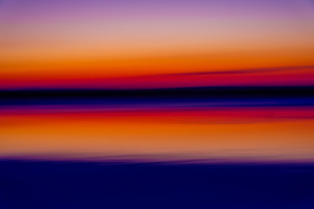 Stunning abstract image of a sunset over an ocean, displaying vibrant hues of orange, red, and purple in a blurred, ethereal landscape.の写真素材