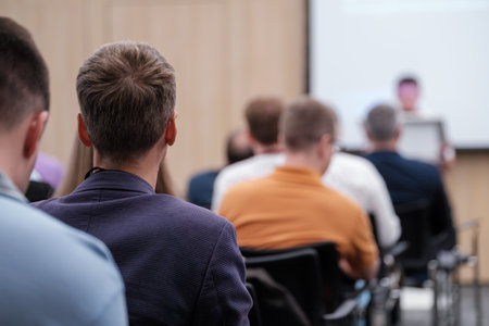 People sitting and listening attentively at a tech conference. Focus is on the back of attendees...
