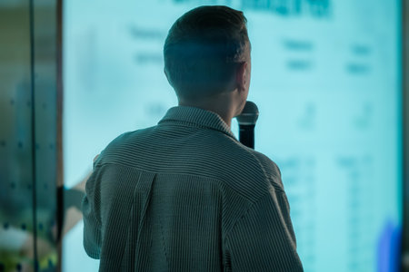 Rear view of a speaker presenting a business report on a large screen in a professional setting. The...