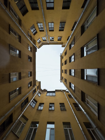 A perspective shot looking up at a yellow apartment buildings courtyard, with multiple windows and clear sky overhead.の写真素材