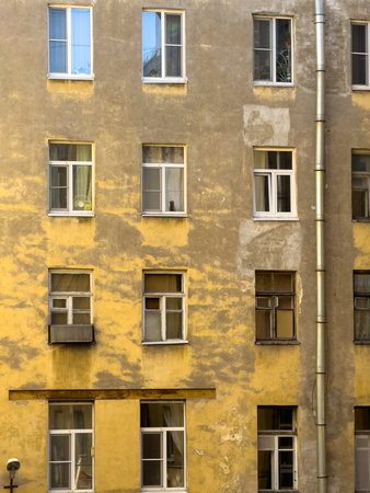 Facade of an old apartment building with weathered yellow walls and various windows. The aged...