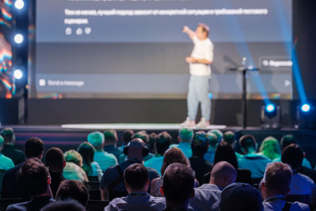 Business professional presenting at a conference with a large audience, highlighting key points on a screen.の写真素材
