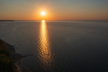 Tranquil sunset casts a golden glow over the calm ocean, reflecting peace and serenity. Perfect for backgrounds and nature themes.の写真素材