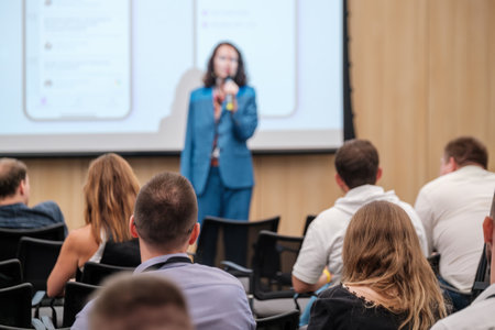 Speaker in blue suit presenting to audience during business meeting, with focus on attendees and blurred backgroundの写真素材