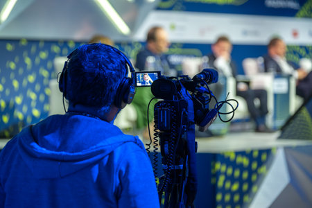 Cameraman recording a business conference with participants in the background. Focus on the...