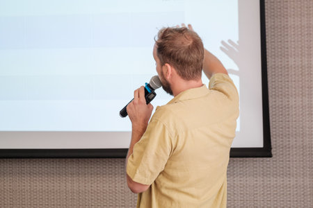 Man presenting with microphone pointing at projection screen during business meeting or seminar
