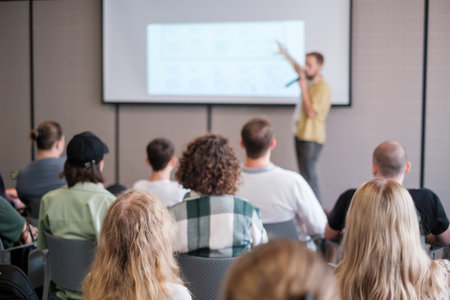 Speaker presents to attentive audience in corporate seminar. Attendees focus on presentation content in a professional setting with modern equipment.の写真素材
