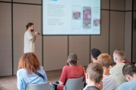 Audience listens to speaker during presentation in modern conference room setting with focus on learning and engagementの写真素材