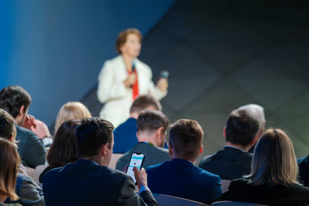 Audience members listening to a speaker during a business conference. Professionally dressed individuals engaged in a formal presentation.の写真素材