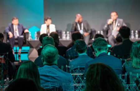 Attendees focus on speakers during business conference panel discussion with emphasis on engagement and networking.の写真素材