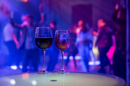 Two glasses on table at nightclub with vibrant background. Energetic party scene features dancing...
