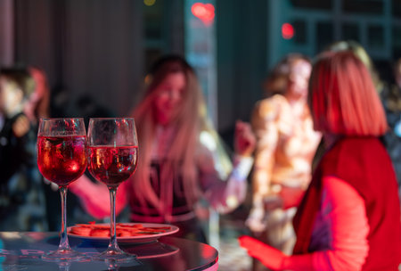 Two glasses of red wine and a plate in front of a blurred party scene with people.の写真素材
