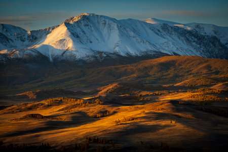 Golden autumn sunlight illuminating Altai mountains creating stunning landscape with snow peaks and warm hues of valley below.の写真素材