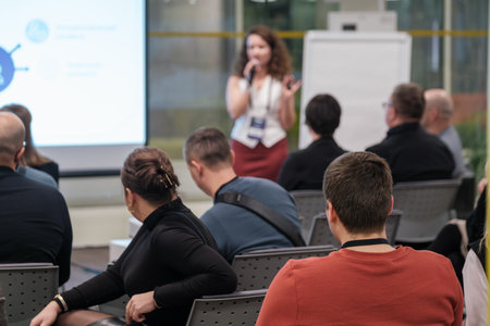 Audience listens to a speaker during a business seminar. A projector screen is visible.